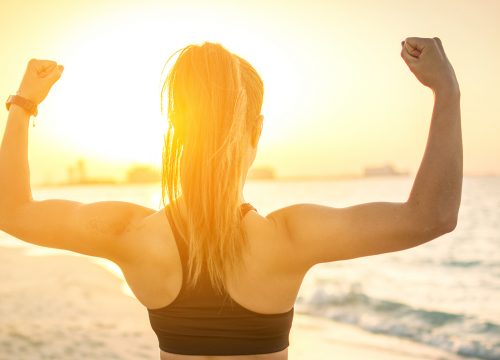 A woman on the beach flexing in front of the sunrise